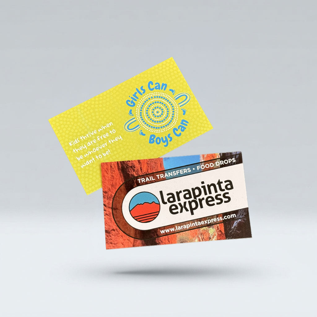 Two printed cards floating on a light gray background: one yellow card with blue text reading 'Girls Can Boys Can' and one rectangular Larapinta Express card with red, white, blue, and black graphics.