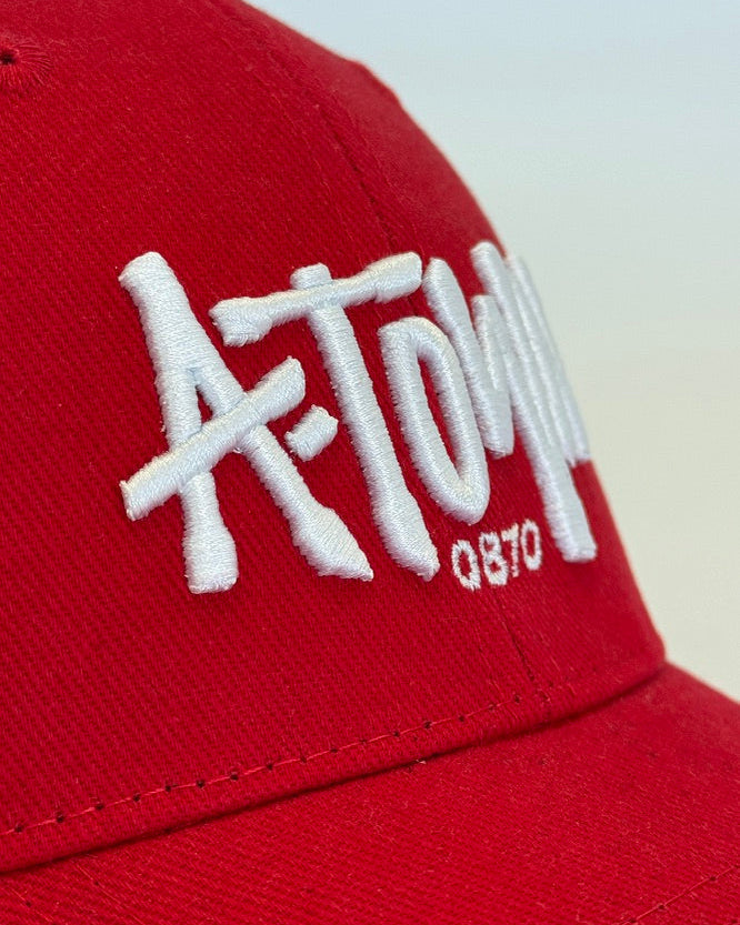 A close-up shot of a red baseball cap featuring white embroidered text that reads 'A-TOWN QSTO' on the front panel.